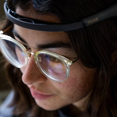 A student uses a bubble fidget while reading on a laptop. A full-spectrum LED lamp sitting on a textbook shines toward her.